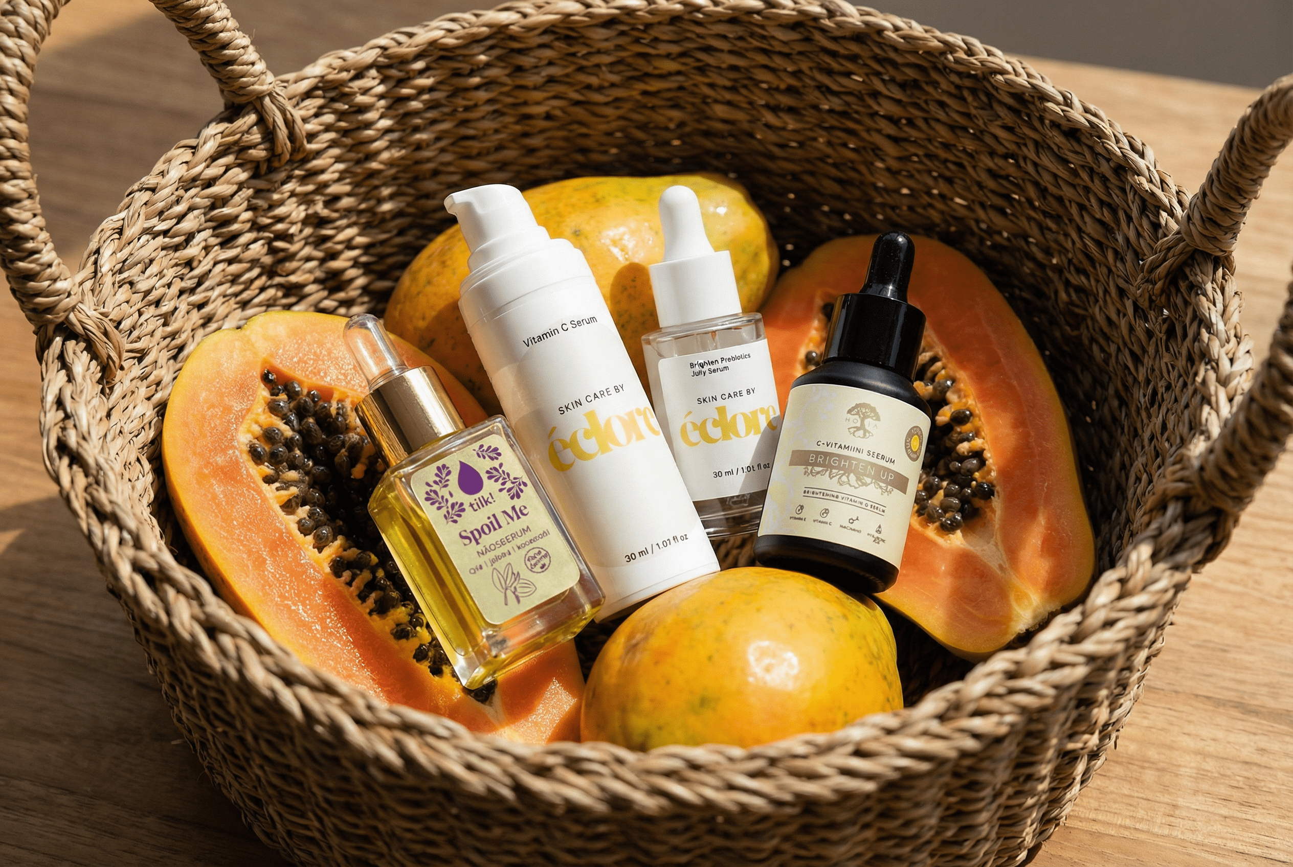 Olika typer av ansiktsserum och lystergivande ansiktsoljor arrangerade med färsk papaya i en flätad korg. Naturlig hudvård för ansiktet med ingredienser som Vitamin C och prebiotika.