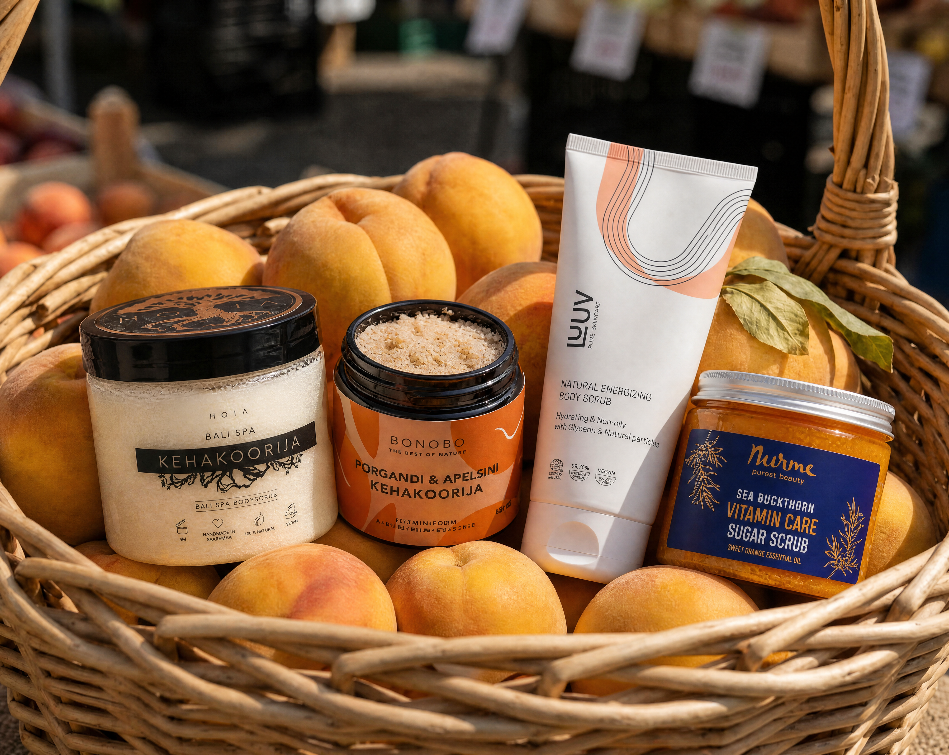 Fyra naturliga body scrubs – HOIA, BONOBO, LUUV och Nurme – i en vidjekorg med persikor
