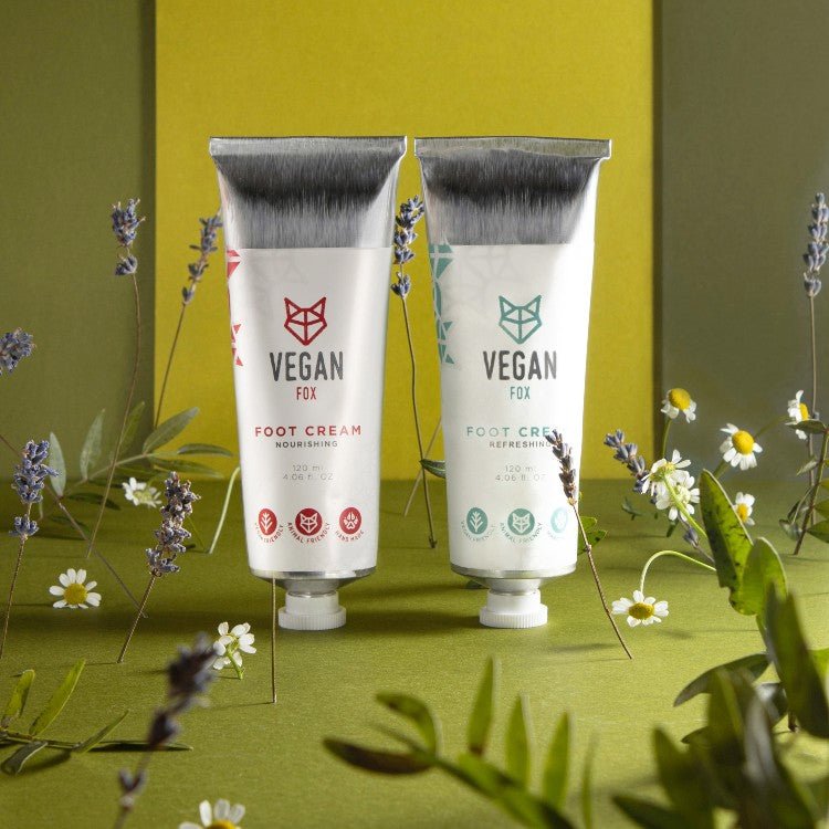 Två vita tuber med Vegan Fox fotkräm 120 ml, en med röda och en med gröna detaljer, omgivna av lavendel och kamomillblommor