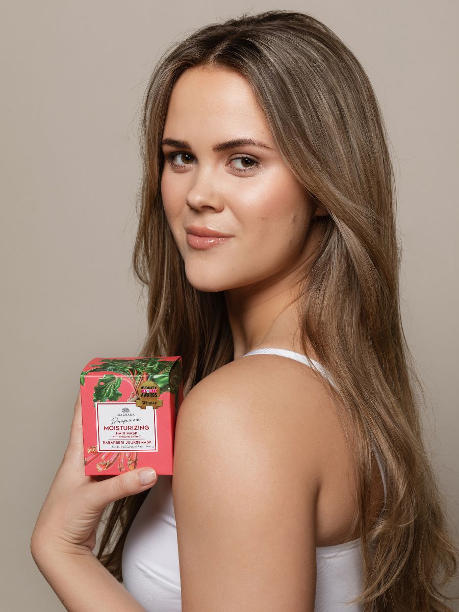 Rosa förpackning med gröna blad-motiv för hårinpackning med rabarber och ricinolja, kvinna håller produkten