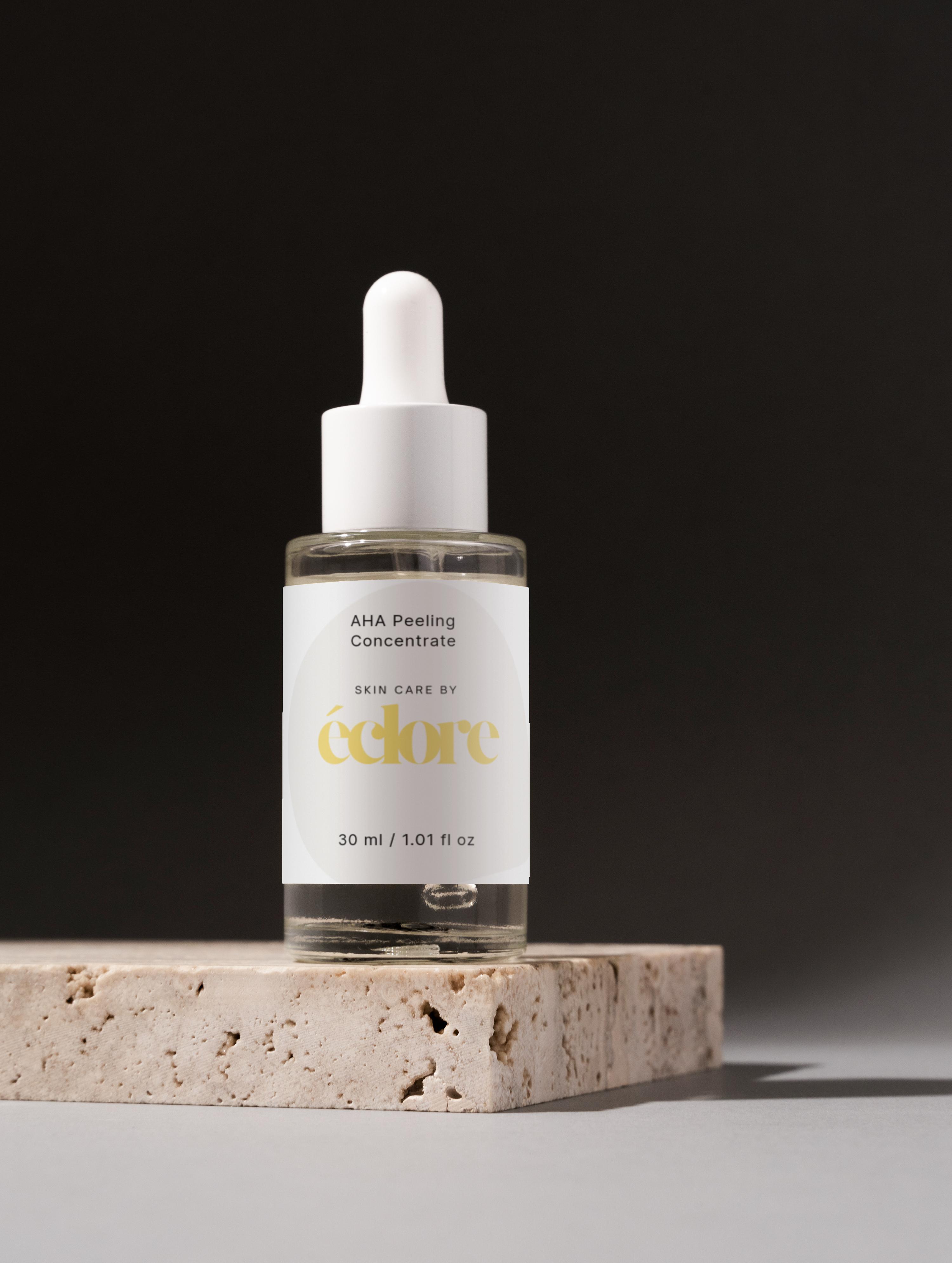AHA Peeling Concentrate i 30ml glasflaska med vit droppipipett och etikett, på porös stenblock mot svart bakgrund
