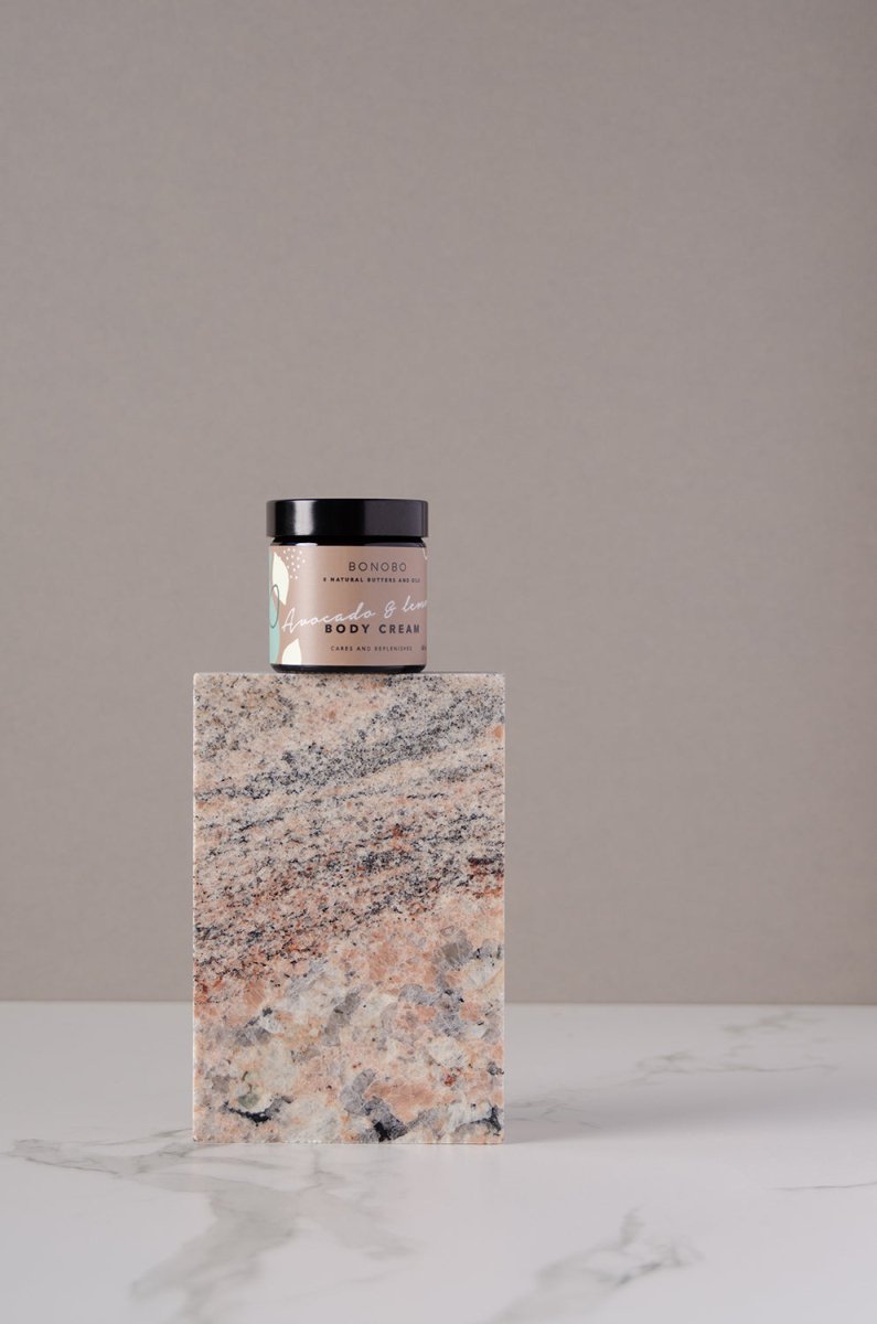 Bonobo Body Cream i glasburk med svart lock, ljusrosa etikett, står på marmorsockel mot neutral bakgrund