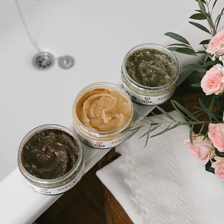 Tre öppna burkar med body scrub i olika nyanser - grön, beige och mörkgrön textur med naturliga ingredienser