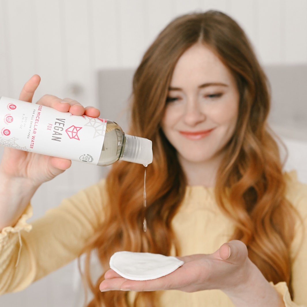 Kvinna häller Rose Micellar Water från vit flaska med rosa detaljer i handflatan - ansiktsrengöring