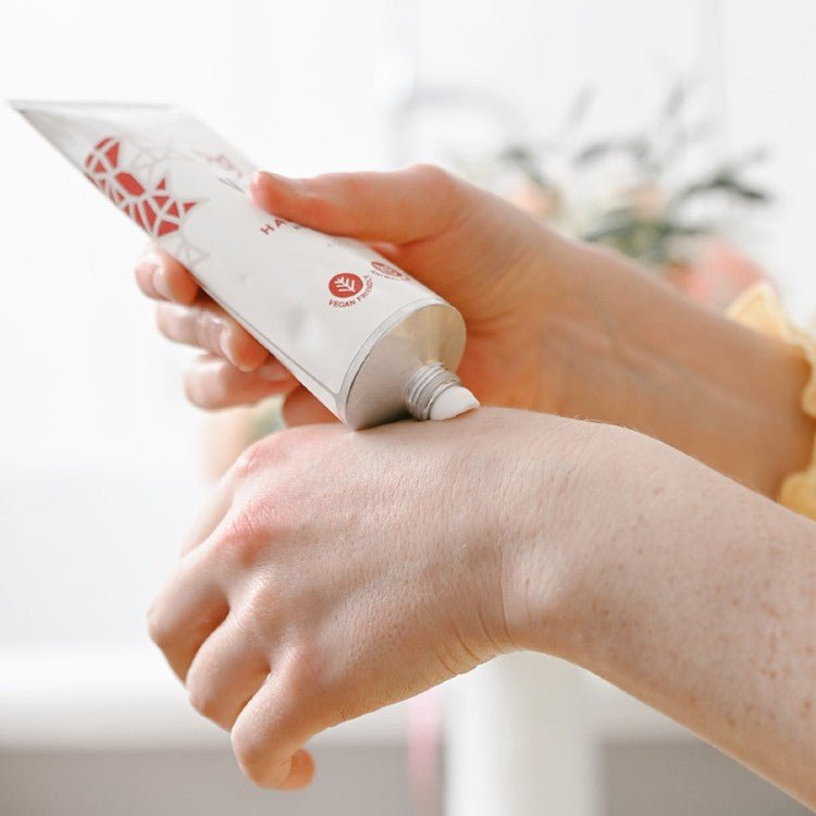 Närande handkräm med sheasmör i vit tub som klämts ut på hand, krämig vit textur syns på huden