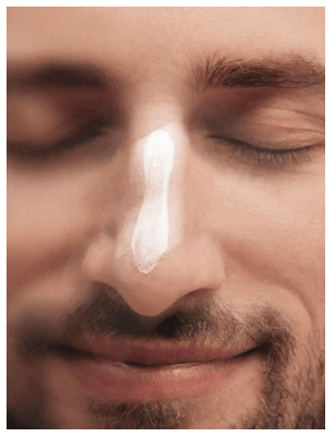 Man med stängda ögon och ett streck vit hyaluronic acid face cream på näsan, visar hudvårdsprodukten i användning