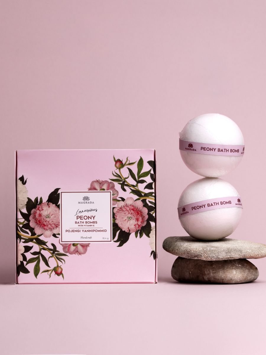 Rosa förpackning och vita runda badbomber med text Peony Bath Bomb, staplade på stenar mot rosa bakgrund