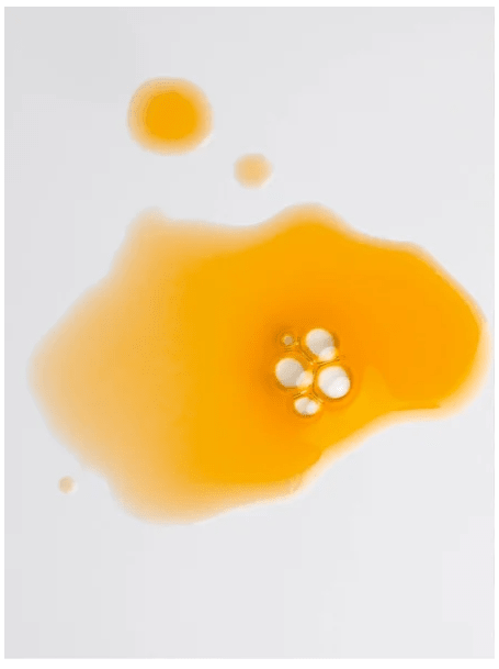 Gul honungsfärgad olja i droppar och större pöl som visar texturen hos Nourishing Facial Oil 30 ml