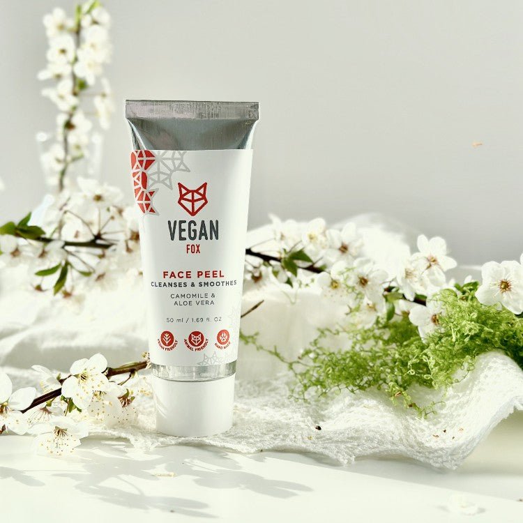 Vegan Fox Face Peel 50ml i vit tub med röd logotyp, omgiven av vita blommor och gröna växter på vit bakgrund