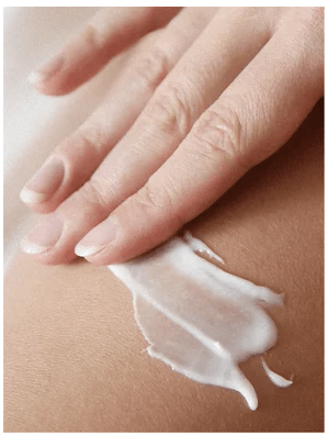 Hand applicerar vit krämig Sensitive Skin Body Cream på huden, visar kremets mjuka textur och smidiga konsistens