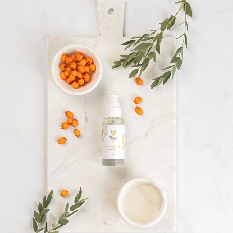 Face Serum med Hyaluronic Acid i klar glasflaska med vit pumpspray, omgiven av havtorn och olivkvistar på marmorbakgrund