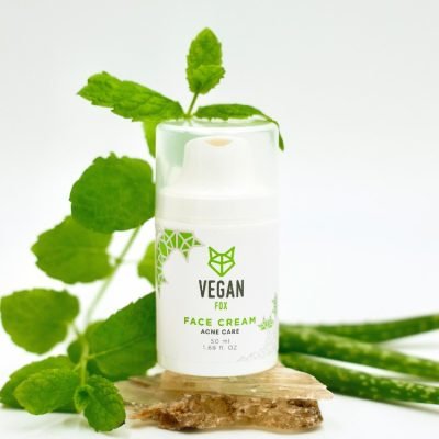 Vit cylinderformad burk med Acne Care Face Cream omgiven av gröna växter och aloe vera på träbakgrund