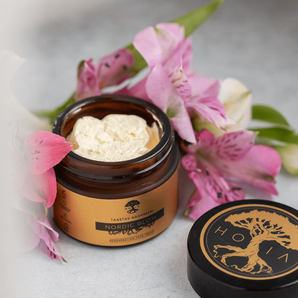 Öppen burk med Ansiktskräm Nordic Glow, krämig konsistens, bland rosa blommor