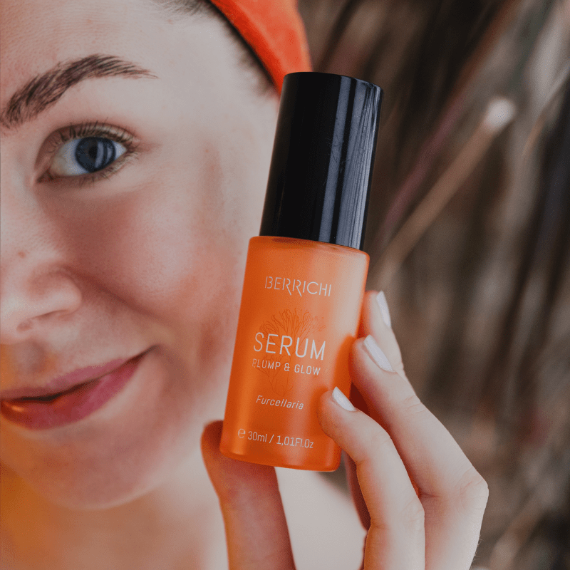 Orange återfuktande serum 30ml i glasflaska med svart pump, hålls av kvinna med naturlig hudvård