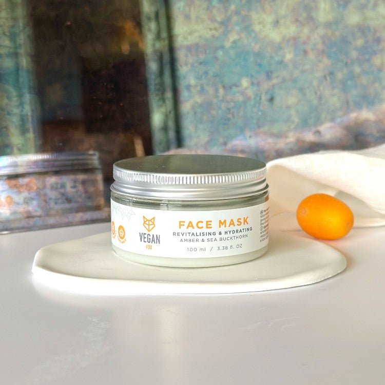 Revitalising & Hydrating Face Mask i vit burk med silverfärgat lock, 100ml, placerad på vit tallrik med orange frukt