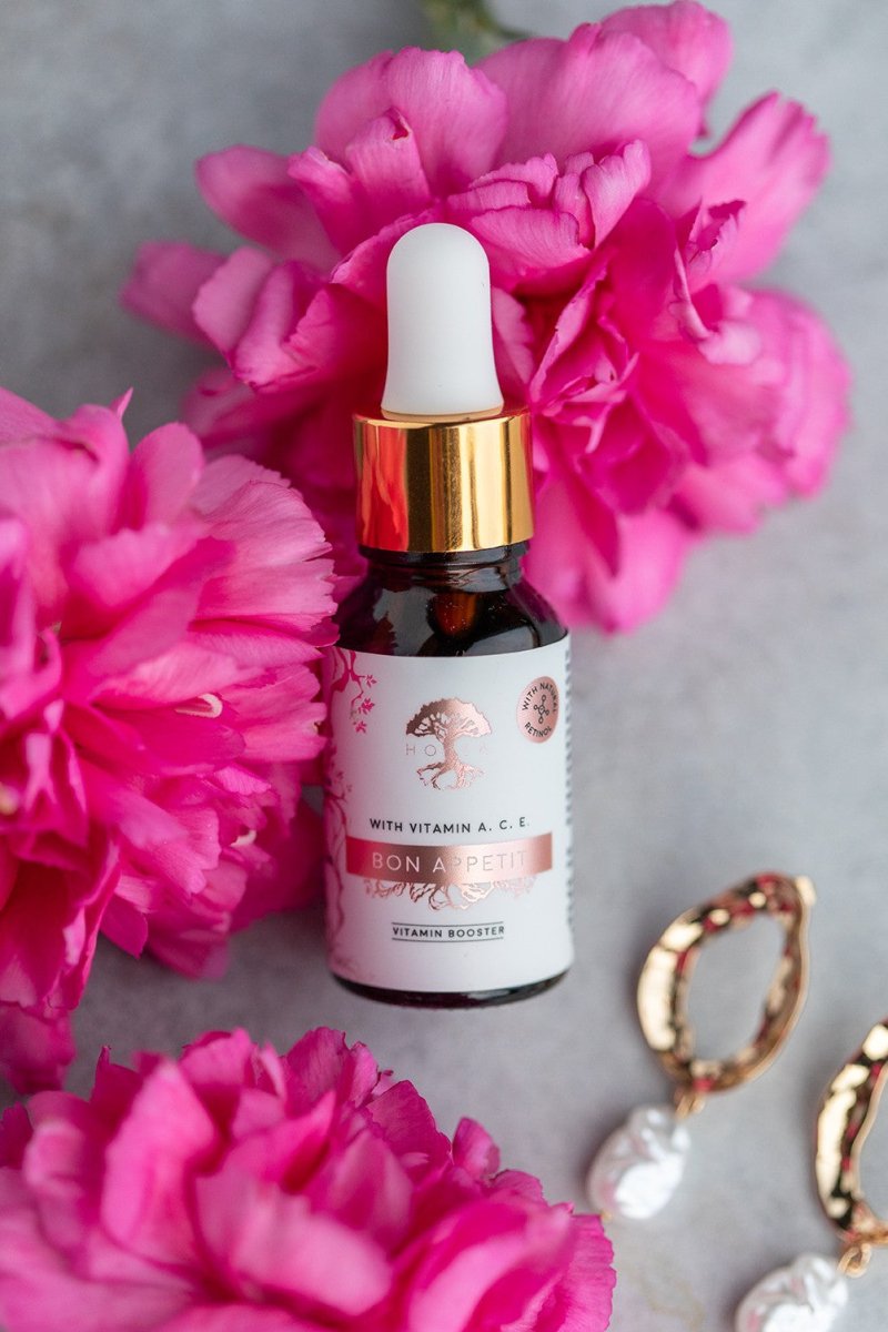 HOIA bakuchiolserum i brun droppflaska med guldpipett bland rosa pioner