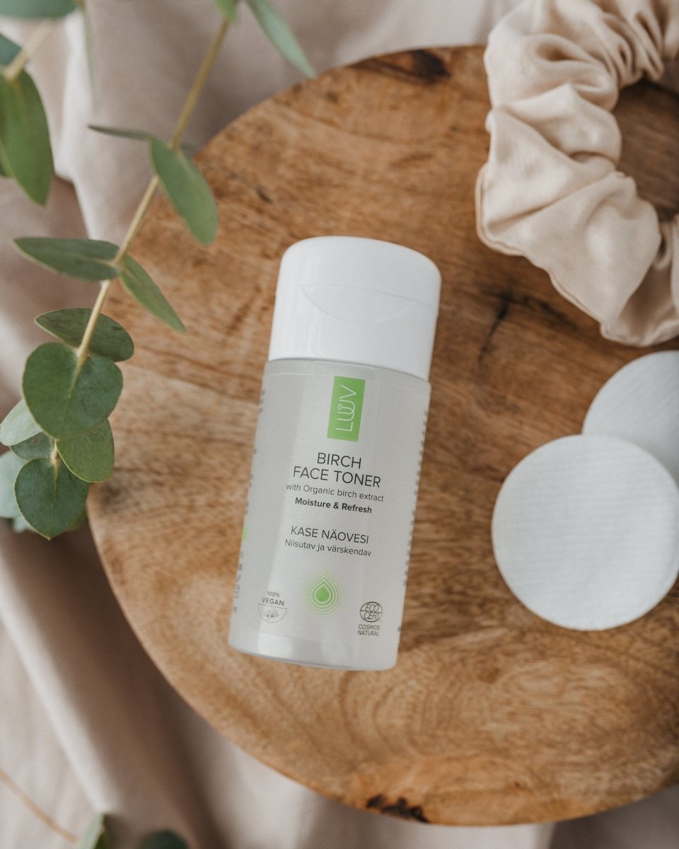 Vit flaska med Björk Ansiktstoner på träbricka omgiven av eukalyptusblad och beige textil