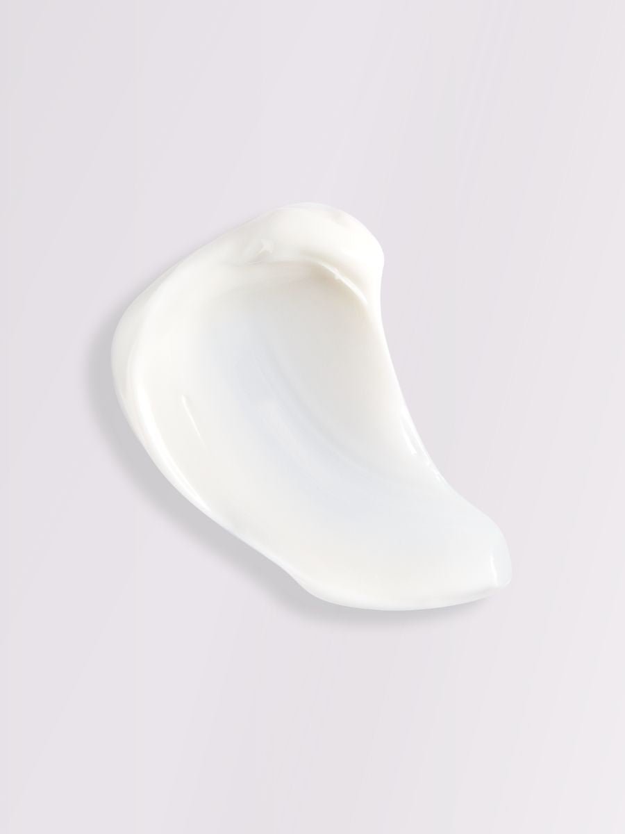 Vit krämig textur av Body Cream Pion & Kvitten utstruken på ljus bakgrund, visar krämens mjuka konsistens