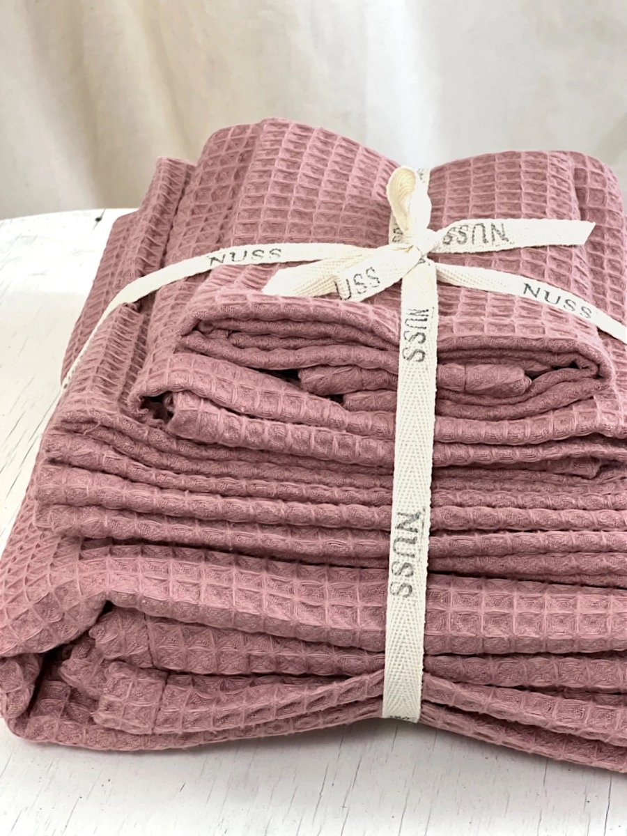 Hopvikta bomullshandduk våffla i old pink, buntad med vitt band, på vit stol
