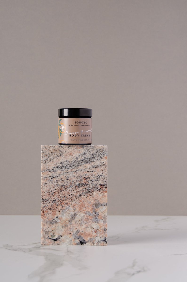 BONOBO Body Cream Orange & carrot i glasburk med svart lock, placerad på marmorblock mot neutral bakgrund