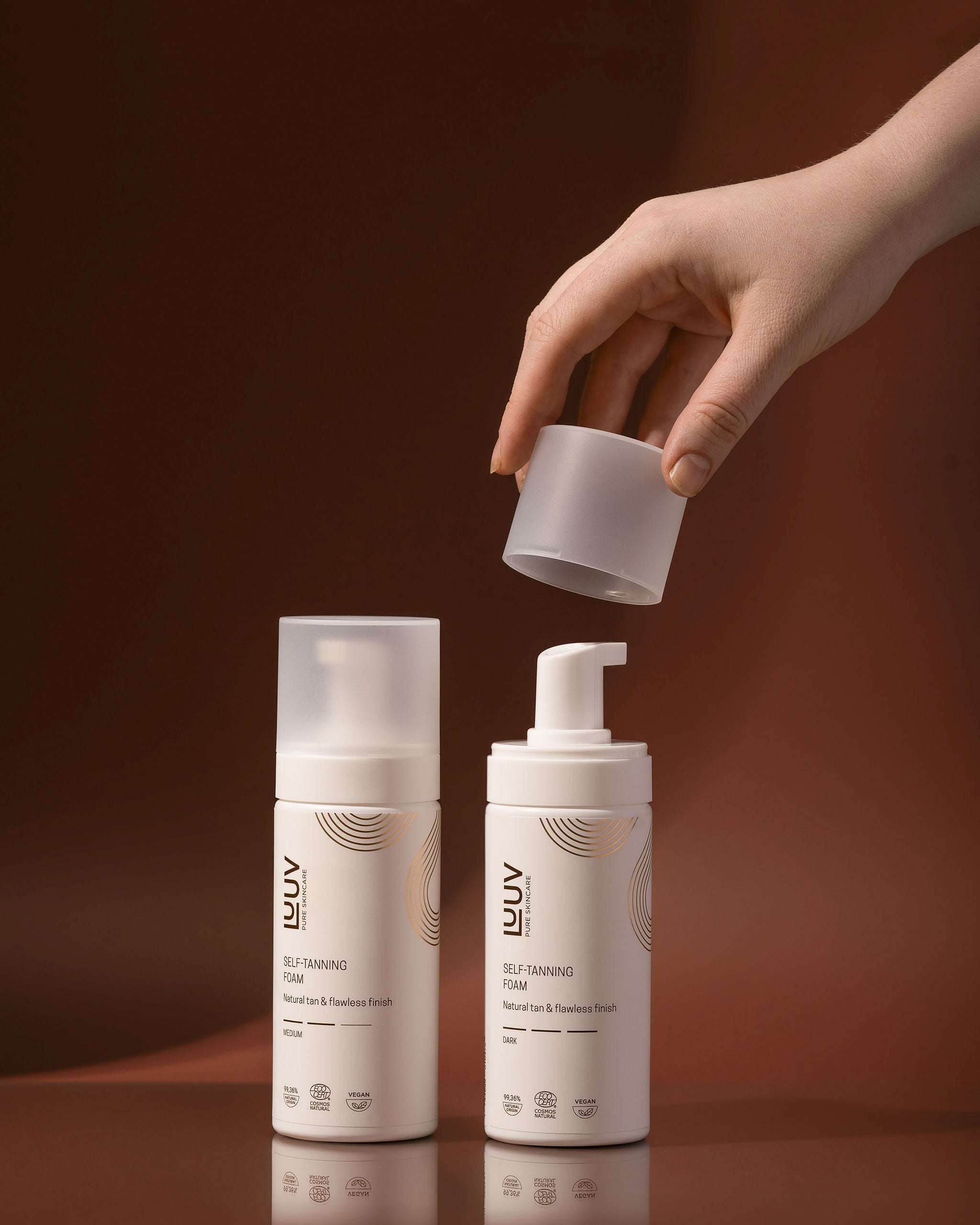 Brun Utan Sol Foam Medium i vit flaska med pump, hand som håller genomskinligt lock, brun bakgrund