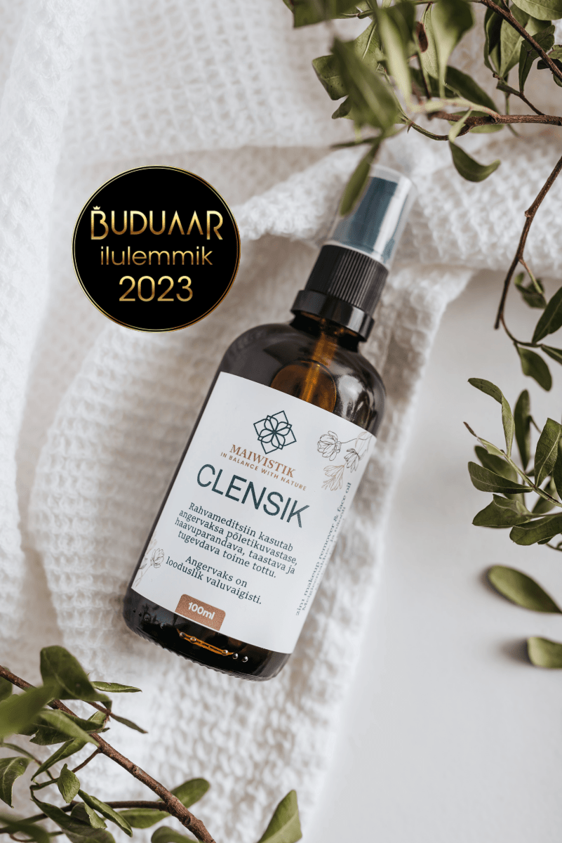 CLENSIK Make-up Removal Oil i brun glasflaska med spraytopp, omgiven av gröna kvistar på vit textilbakgrund