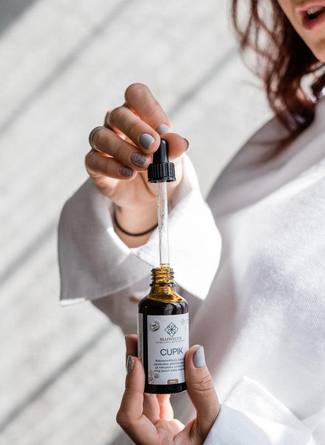 Kvinna håller CUPIK Oregano och Rölleka olja 50ml i brun glasflaska med pipett, droppande genomskinlig olja