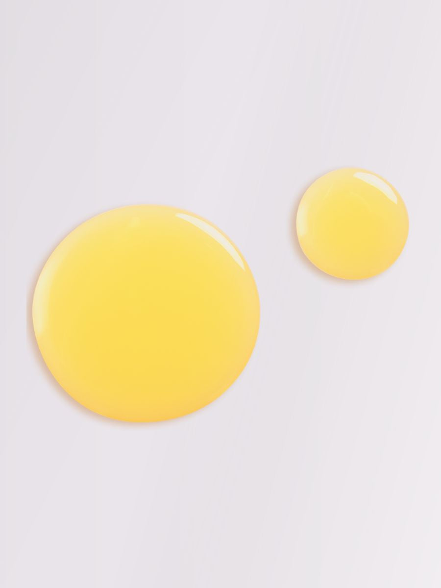 Två gula cirklar av duscholja med pion och ekologiska fruktoljor på ljus bakgrund, visar oljans gyllene färg