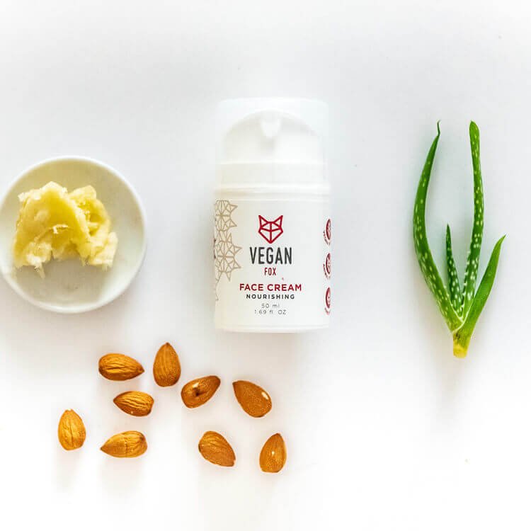 Vit burk med Vegan Fox Nourishing Face Cream 50ml omgiven av mandlar, aloe vera-blad och skål med gul hudvårdskräm