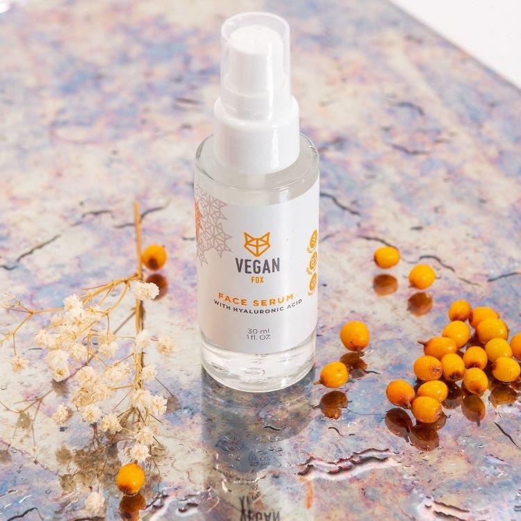 Vegan Fox Face Serum med Hyaluronic Acid i genomskinlig glasflaska med vit pumpspray, omgiven av torkade blommor