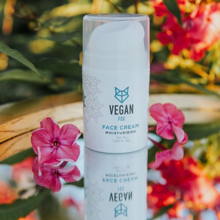 Vit cylindrisk tube med Vegan Fox Moisturising Face Cream 50ml omgiven av rosa blommor på spegelbord