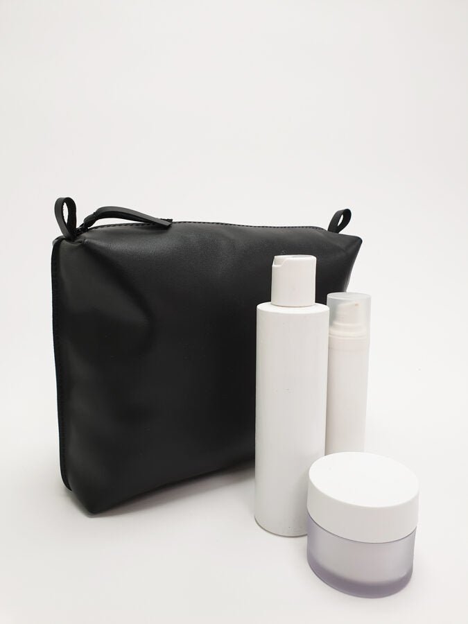 Handgjord necessär i svart läder Large med vita hudvårdsprodukter - flaska, spray och burk framför necessären