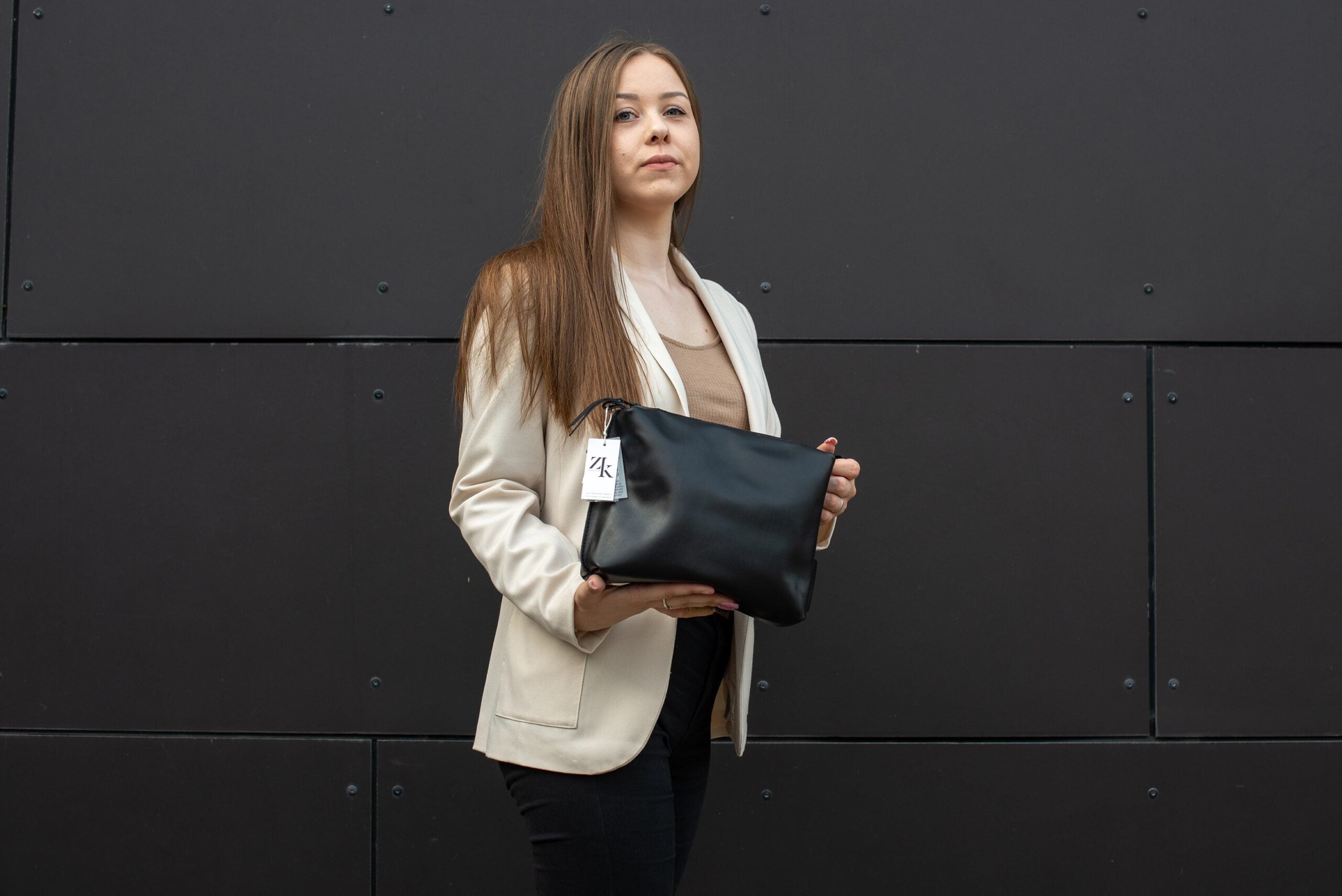 Handgjord necessär i svart läder Large - elegant svart läderväska med vit etikett hålls av kvinna i beige kavaj