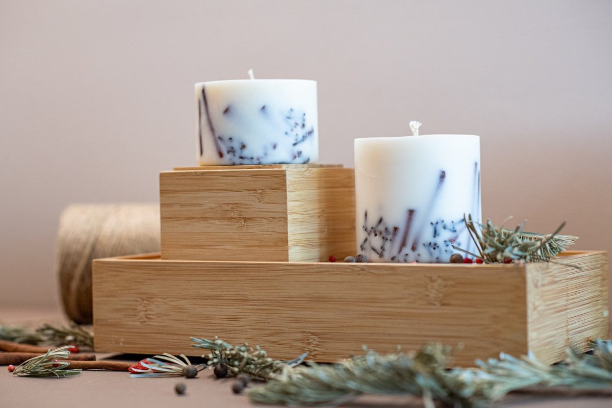 Handgjort sojavaxljus med kaneldoft i vit cylinderform med blåa mönster, placerat på bambulåda med granris