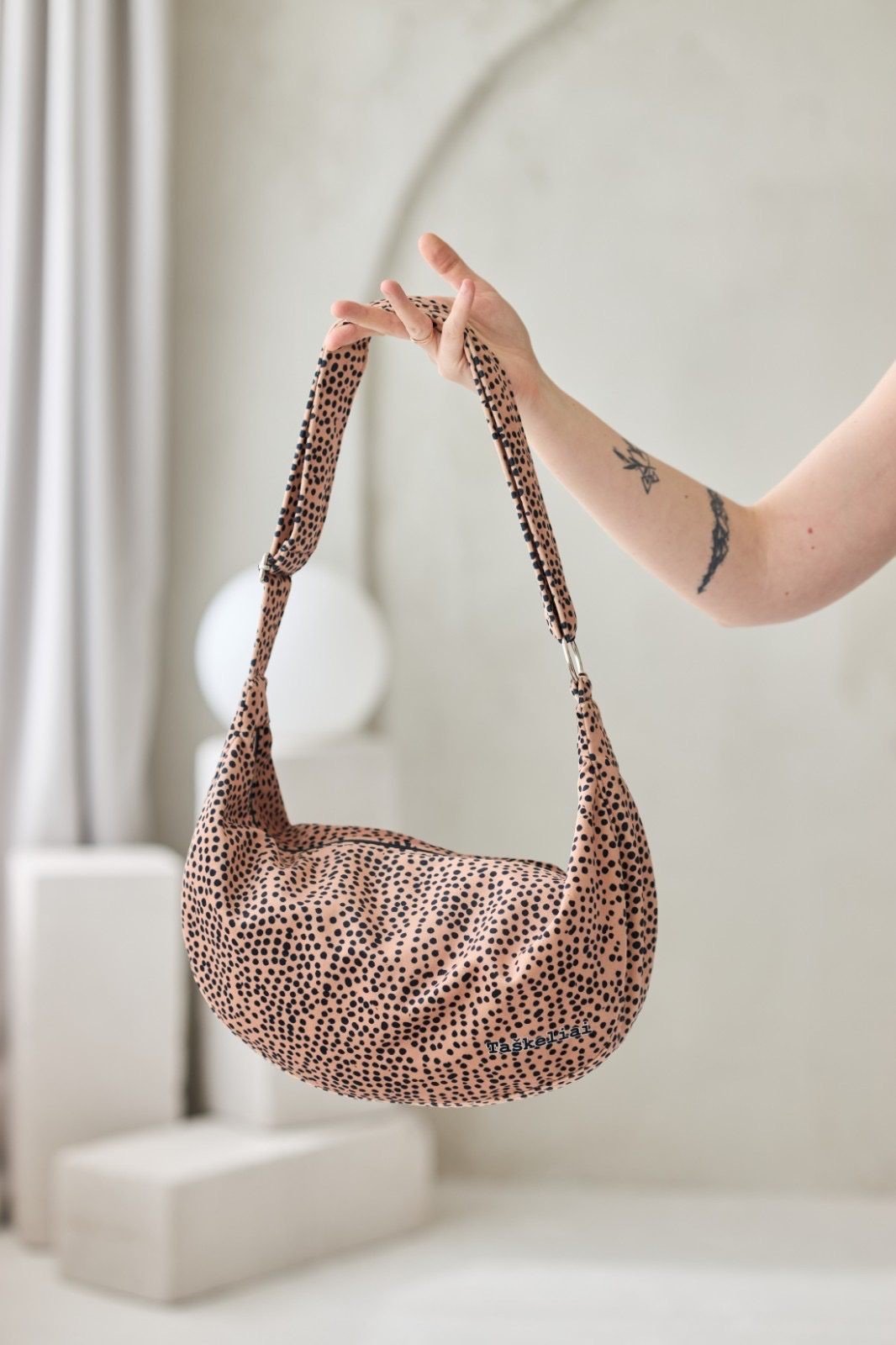Hobo Bag Cream and Dots - beige väska med svarta prickar hålls upp av händer med tatueringar mot vit bakgrund