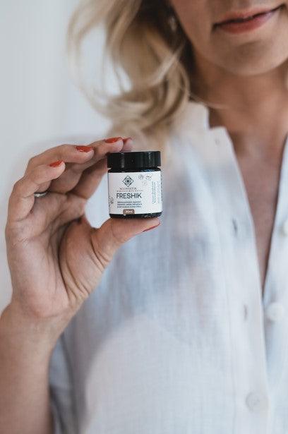 Kvinna i vit skjorta håller upp en liten vit burk med svart lock - Kamomill Cream Deodorant 30ml från éclore