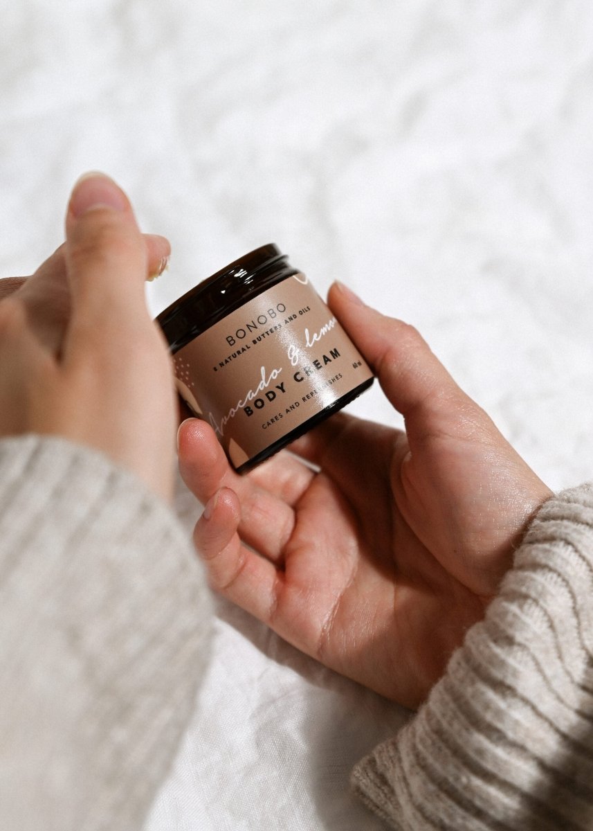 Händer håller en liten brun burk med Bonobo Body Cream Avokado och Citron mot ljus bakgrund