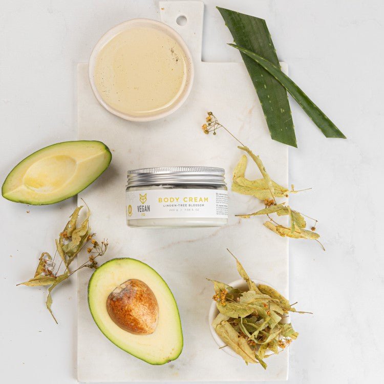 Lindblomma body cream i glasburk omgiven av avokado, aloe vera, torkade lindblommor och en skål med kräm