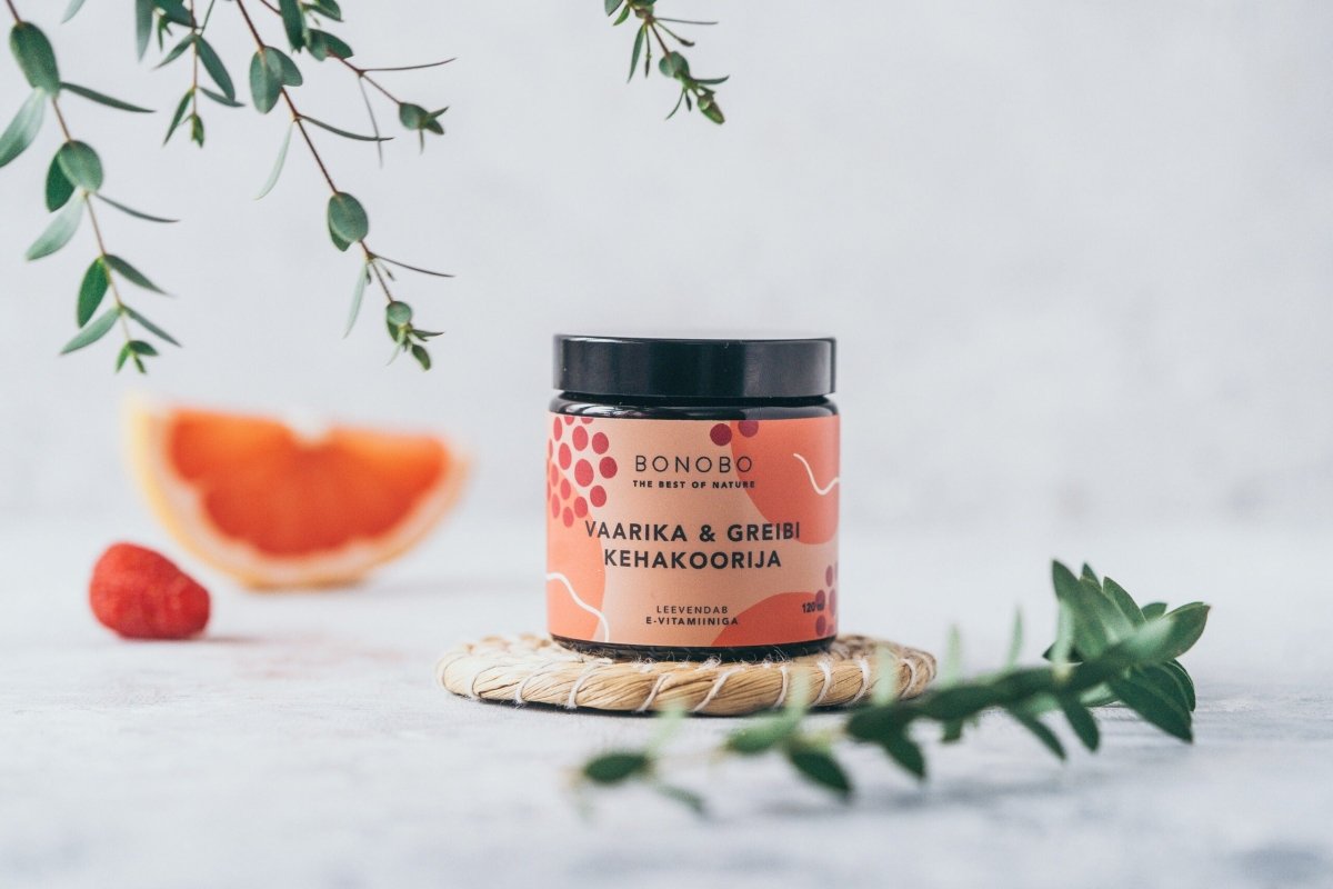 BONOBO kroppsskrubb med hallon och grapefrukt i mörk glasburk, omgiven av grapefruktklyfta, hallon och gröna kvistar