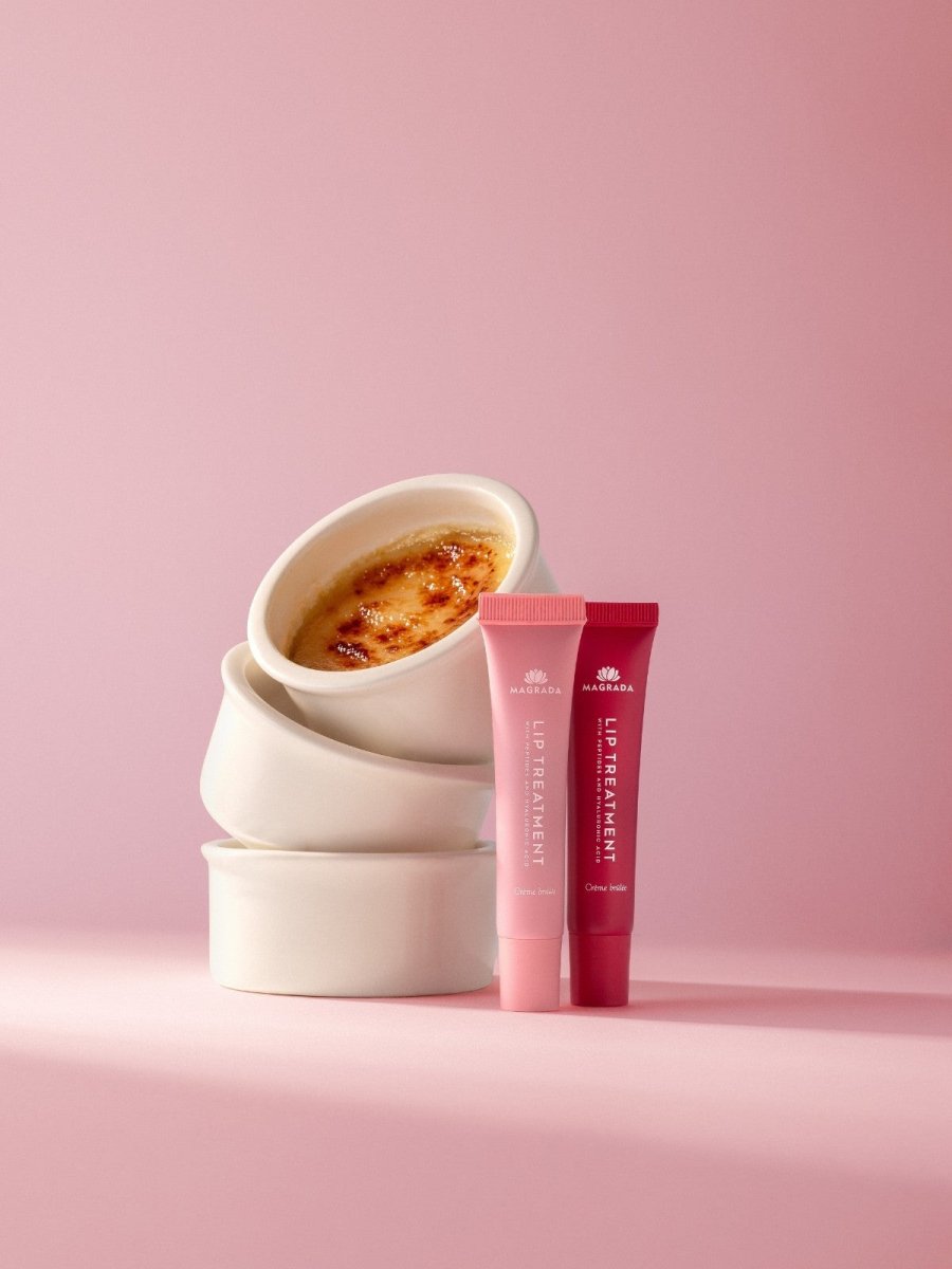 Två tuber läppbalsam med hyaluronsyra i rosa och cerise, uppställda framför staplade skålar med crème brûlée