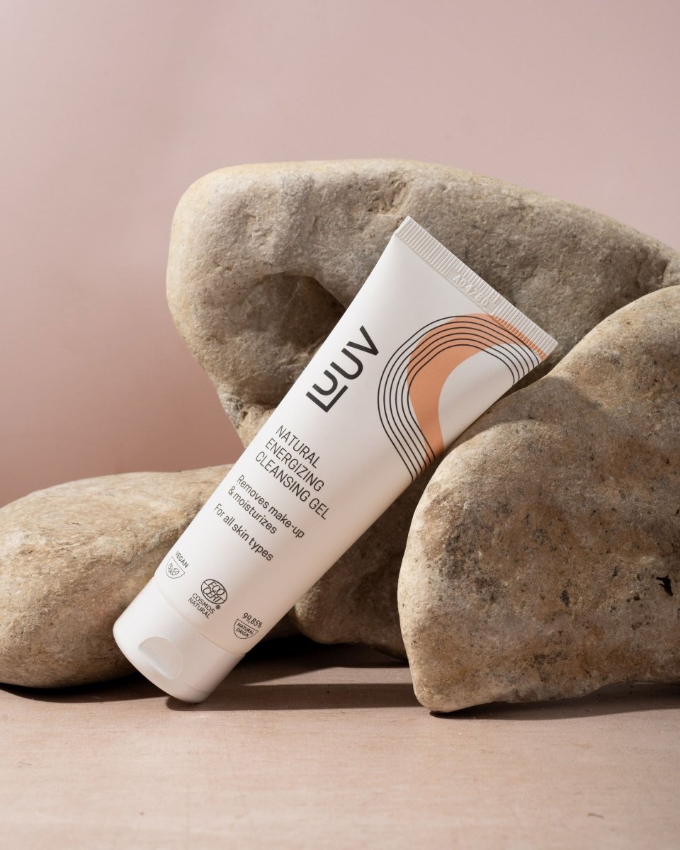 LUUV Natural Energizing Cleansing Gel i vit tub med orange designelement, placerad mot beige stenar på rosa bakgrund