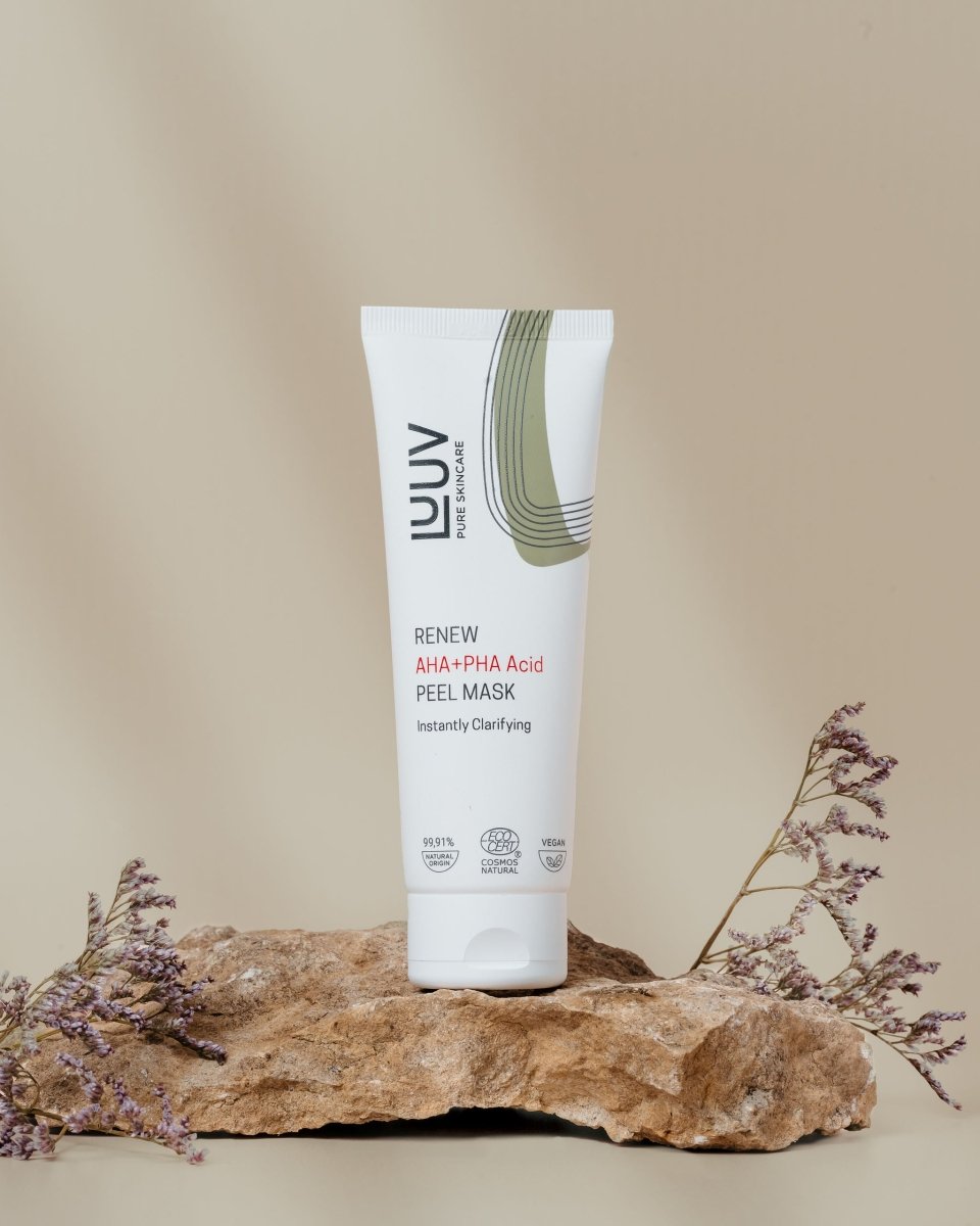 LUUV Renew Peel Mask i vit tub med grön grafisk design, placerad på sandstensblock med torkade lila blommor