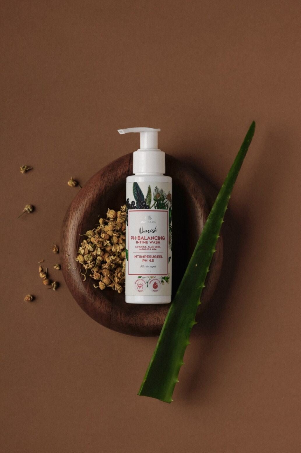 Magrada intimduschgel med kamomill & aloe vera i vit flaska med pump, omgiven av torkade kamomillblommor och aloe vera-blad