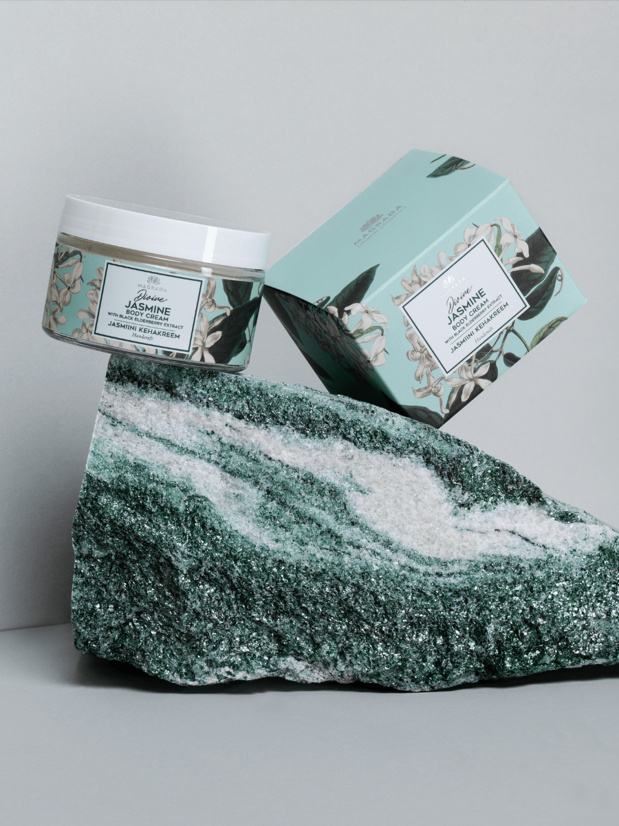 Magrada Jasmine Body Cream med hyaluronsyra i mintgrön förpackning med jasminblommor, vit burk och lock på grön marmor