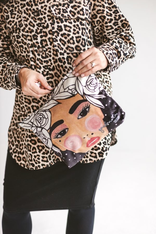 Makeup Bag Pouch Yoko Black - svart necessär med illustrerat kvinnoansikte och vita rosor, hålls av kvinna i leopardmönstrad tröja