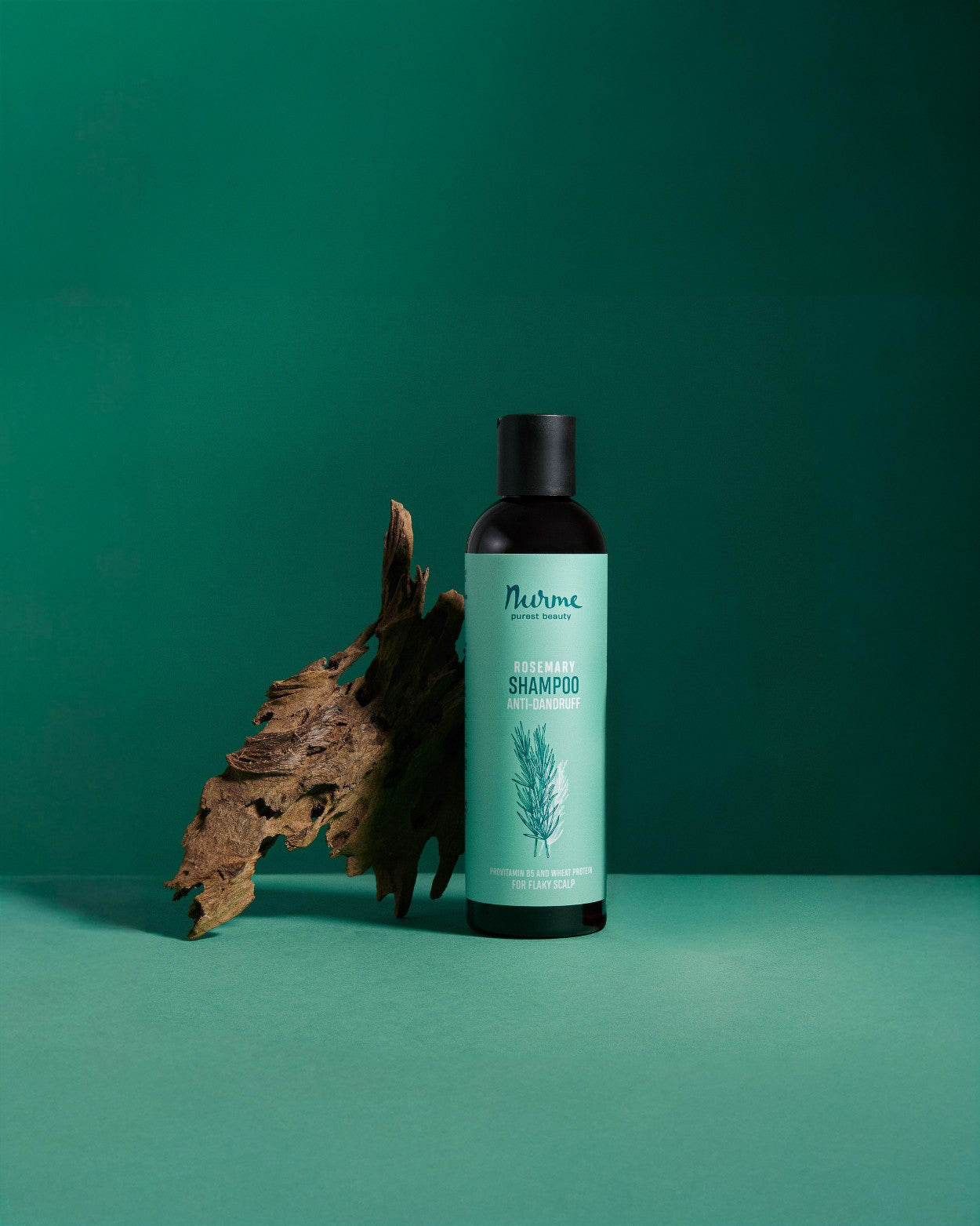 Nurme mjällschampo med rosmarin i grön flaska med svart kork, placerad bredvid träbit mot grön bakgrund