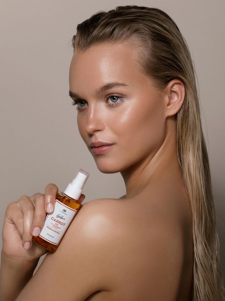 Kvinna håller brun glasflaska med vit pumpspray - Morotolja med Rosmarinextrakt för naturlig hårvård