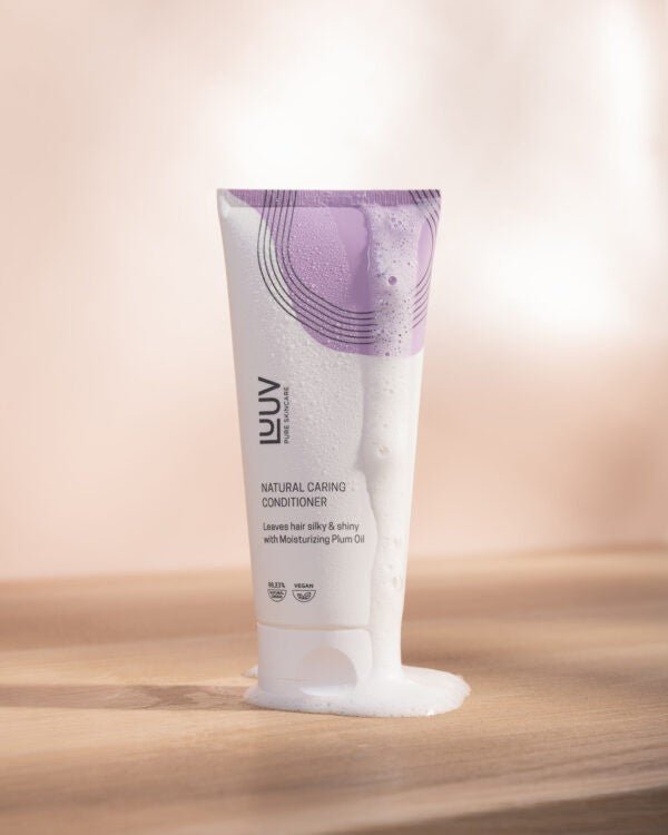 Vit tub med lila grafiska detaljer innehållande Närande Balsam med Plommonolja 200ml, stående på träyta
