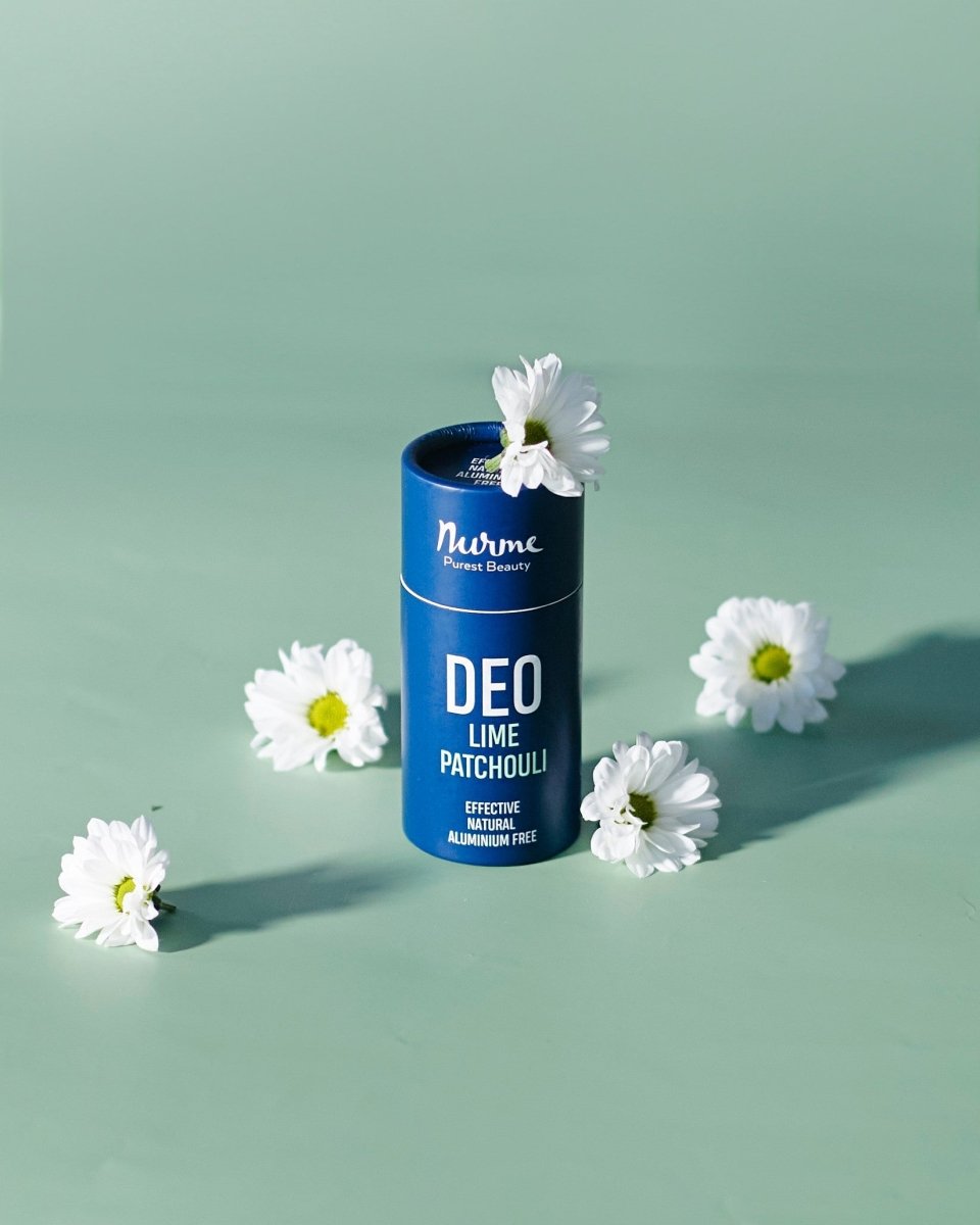 Nurme naturlig deodorant i blå cylinderförpackning med lime patchouli, omgiven av vita blommor på grön bakgrund