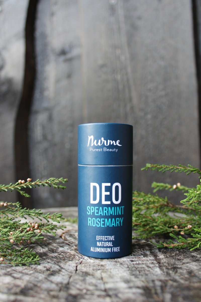 Nurme naturlig deodorant i blå cylindrisk förpackning med vit text, omgiven av gröna kvistar på träunderlag